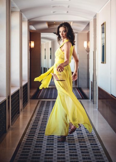 Anja Gockel Fashion Frau in einem langen, gelben Kleid, posierend in einem eleganten Flur.