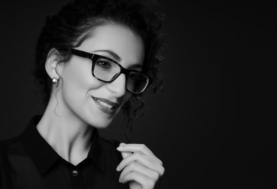 Make-up und Brille Frau mit lockigem Haar, Brille und lächelndem Gesicht vor schwarzem Hintergrund.